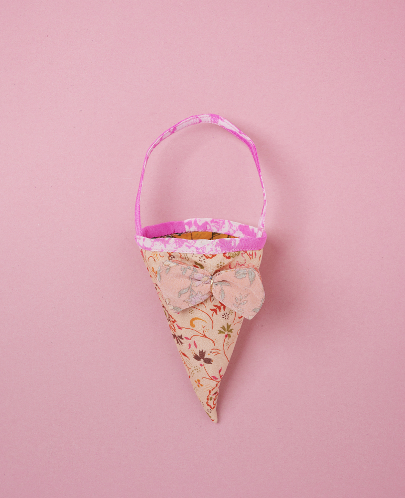 Cornet-SILK-Cornet-Cream Stofftüte in Kegelform, floral gemustert, rosa und beige, dekorative Schleife, Tragegriff, rosa Hintergrund.
