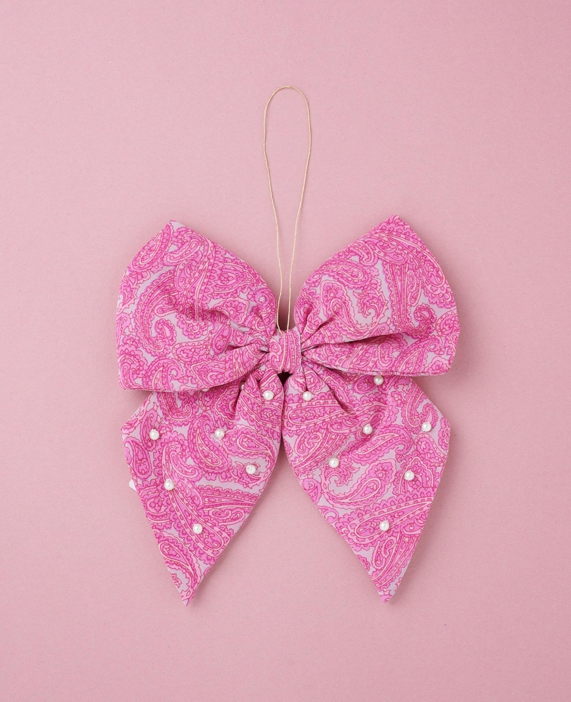 Bow-SILK-Ornament-Taffy Rosa Schleife, Paisley-Muster, Perlenverzierung, flach liegend auf rosa Hintergrund.