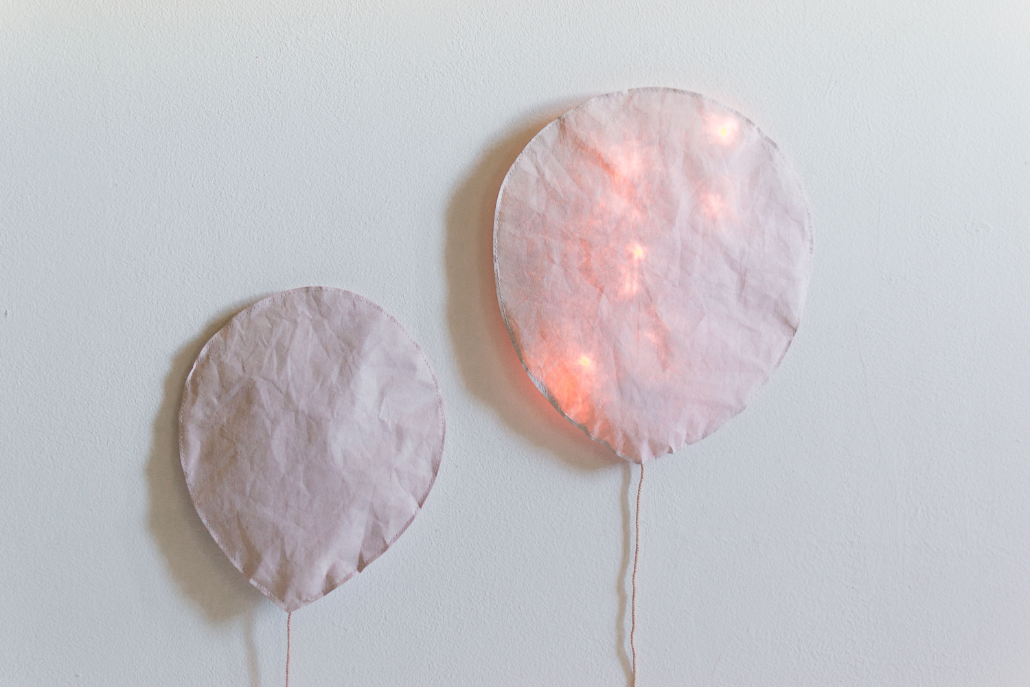 DSC_0712 Zwei Wandlampen in Ballonform, Stoffbezug in Rosa, rechte Lampe mit integrierter Beleuchtung, abstraktes Design, minimalistisch.