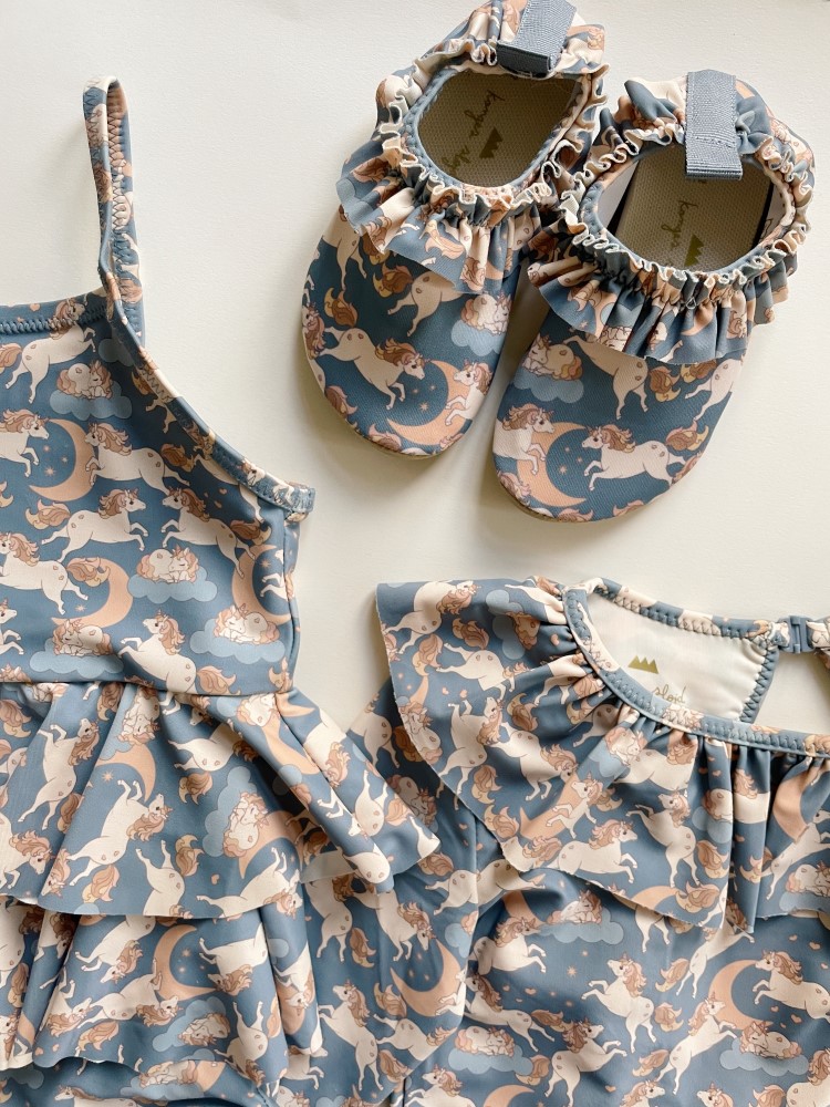 KS4697-MANUCA-FRILL-SWIMSUIT-UNICORN-BLUE-Extra-2 Badeanzug, Hausschuhe und Oberteil für Kinder; Farbe: Blau mit Einhorn- und Mondmuster; Rüschen an den Hausschuhen und am Oberteil.