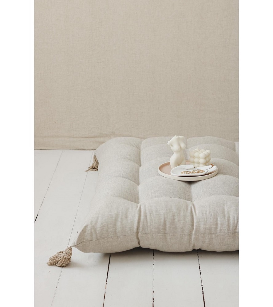 lniany-materac-z-chwostami-naturalny-bez-2 Großes, beiges Bodenkissen mit Quasten; darauf ein helles Tablett mit Figurkerze, Würfelkerze, Schmuck.