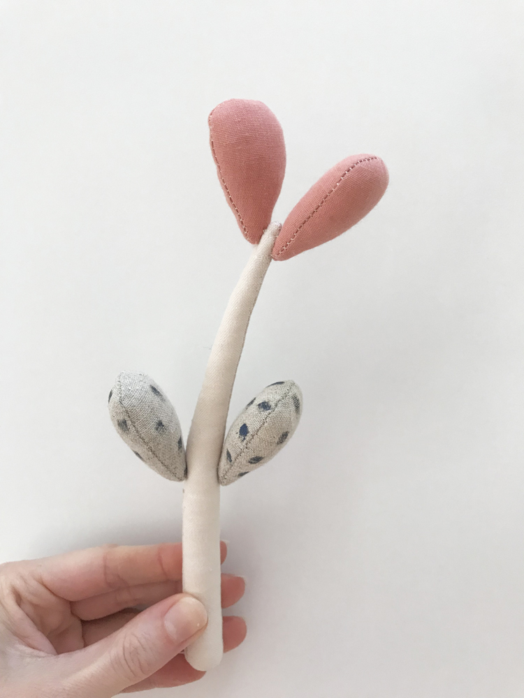 IMG_6289 Stoffspielzeug, beige Stiel, rosa Blätter oben, graue Blätter mit schwarzen Punkten unten, handgehalten.