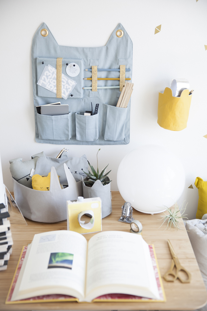 IMG_1313 Wandorganizer aus Stoff, hellblau, goldene Details, diverse Taschen; Tisch mit Buch, Schere, dekorative Aufbewahrungskörbe in Grau und Gelb, Kuscheltier.