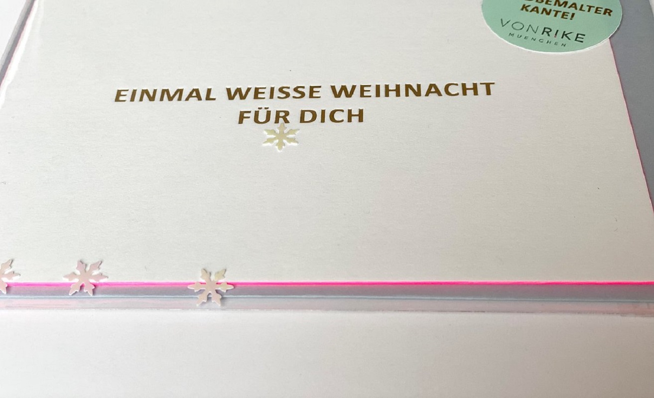 7a75ef_7c3f8b444ada466db7489611b9692fc8_mv2 Weiße Karte, goldener Aufdruck "Einmal weiße Weihnacht für dich", ausgestanzte Schneeflocken, rosa Kante, runder Aufkleber oben rechts.