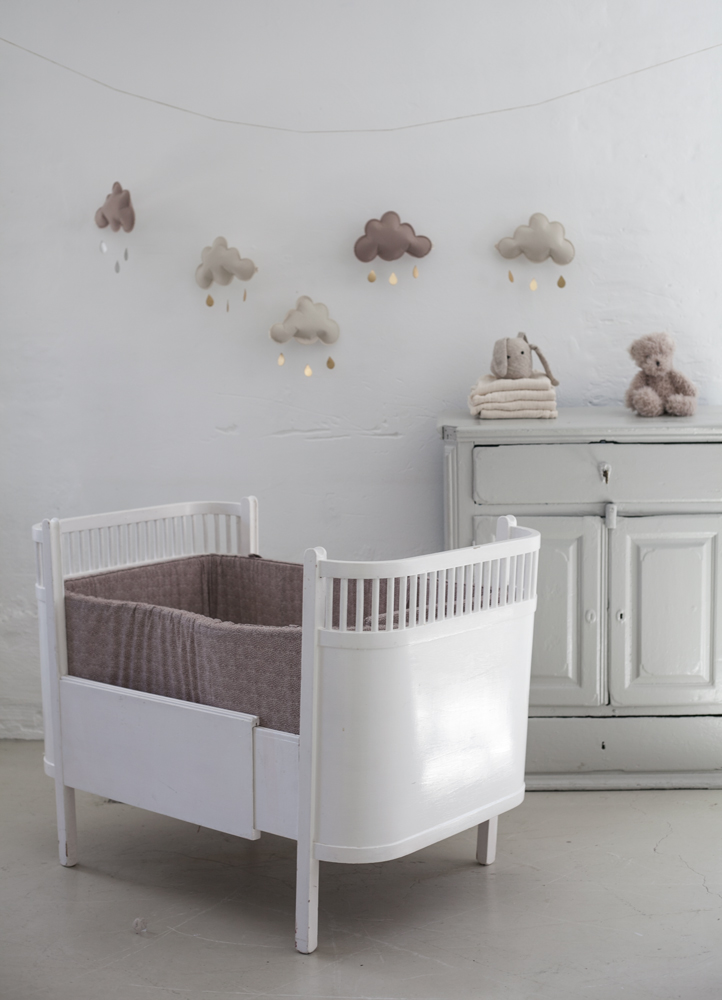 15959ce1692c7f53 Weiße Babywiege, seitliche Gitterstäbe, gepolsterter Einsatz in Beige. Wanddekoration mit wolkenförmigen Mobiles in Braun- und Beigetönen.