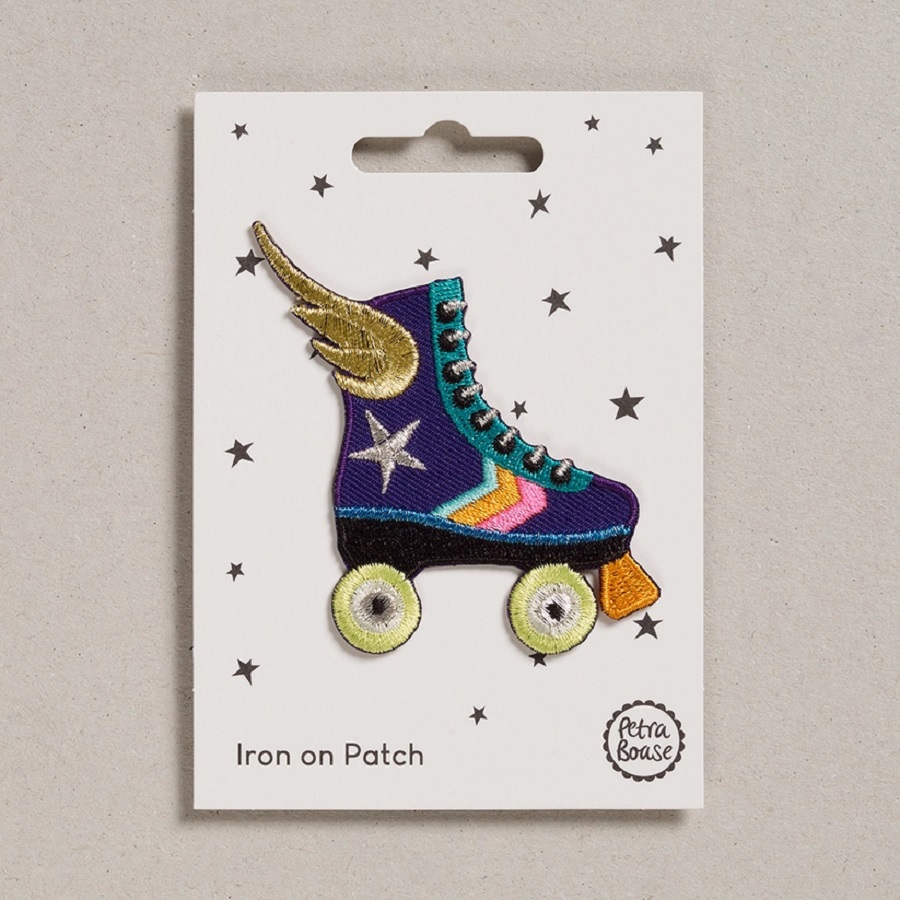 1bcb4a07e45822e8c5881dbe8c35cd6e2ea3a75b2c74fde1f5b3351155805d3a Aufnäher Rollschuh-Design, blau-lila, goldene Flügel, silberner Stern, bunte Streifen, gelbe Räder, Verpackung mit Sternenaufdruck.