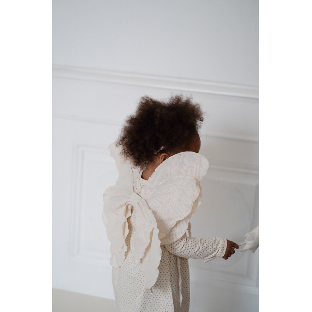 1024x1024-ef2aa0ac73de9b5c0e5265dff2c67812 Kleinkind in cremefarbenem Kleid mit Punkten, trägt große, weiße Engelsflügel.