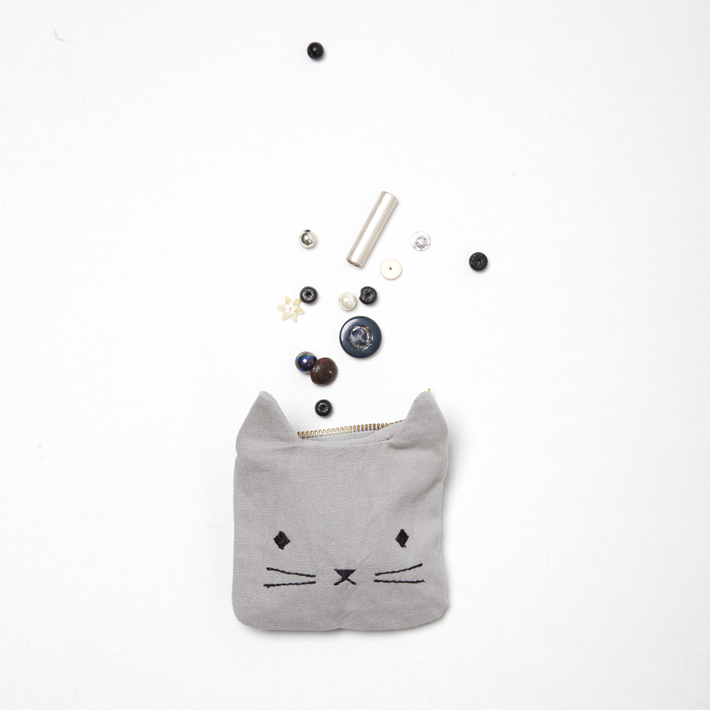 coinpurse-cat-1 Graues Münztäschchen mit Katzenmotiv, Reißverschluss oben, daneben kleine lose Knöpfe und Perlen.