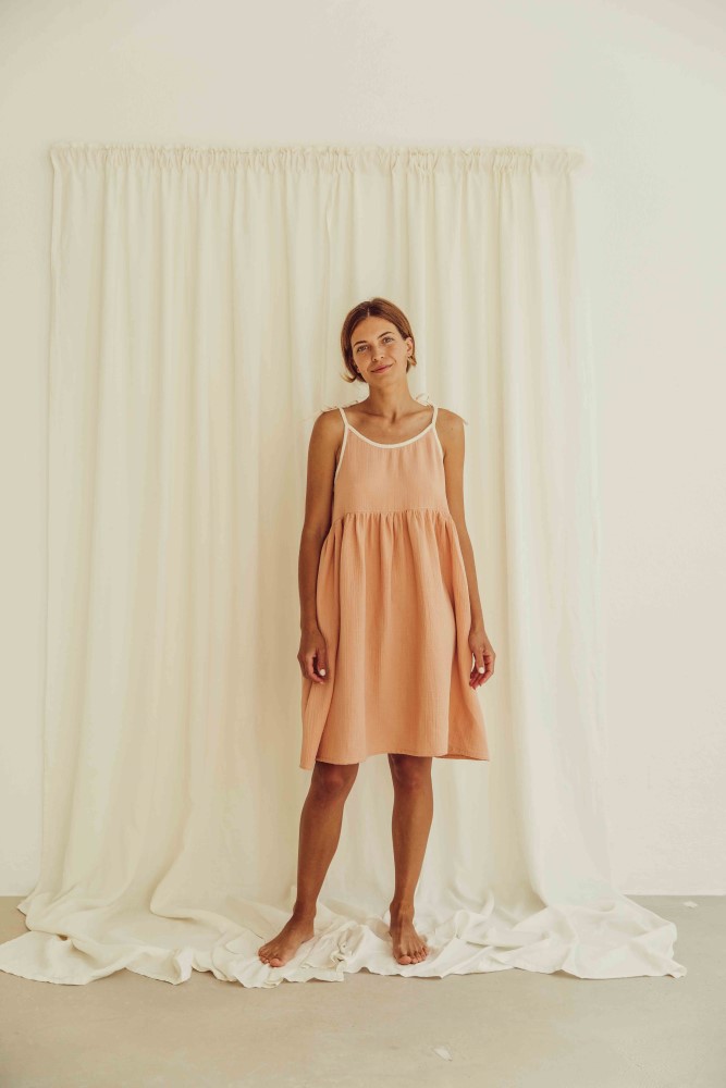 liss23_076_W_louisa-dress_peach_3 Leichtes Sommerkleid, ärmellos, knielang, in Pfirsichfarbe, weiße Träger.