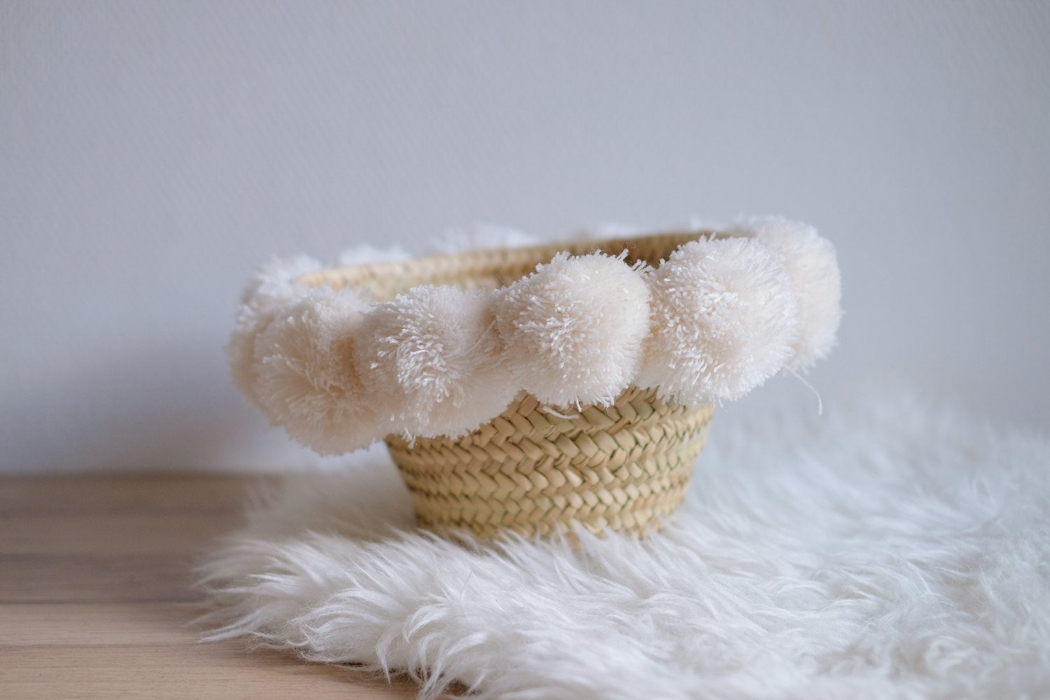 KYRLA_CREAM_1 Geflochtener Korb, hellbraun, mit cremeweißen Bommel-Akzenten am Rand, weiche Textur.