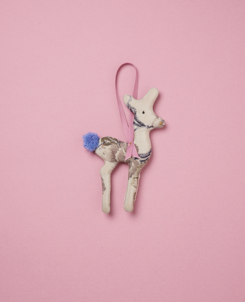 Bambi-SILK-Ornament-Royal-Vanilla Kuscheltier, Rehform, beige mit braunen Mustern, blauer Pompon-Schwanz, rosa Band zum Aufhängen, rosa Hintergrund.