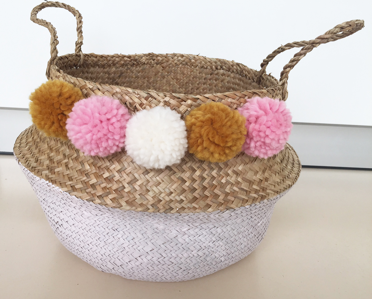 IMG_8925 Geflochtener Korb, Naturton, unterer Teil weiß lackiert, bunte Pompoms in Gelb, Rosa, Weiß.