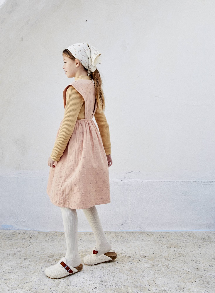 LIAW21_87_pink-sand_side-back Mädchenkleid rosa mit floralem Muster, beige Langarmshirt, weiße Strumpfhose, cremefarbene Pantoletten mit braunen Schnallen, beige Kopftuch mit Blumen.