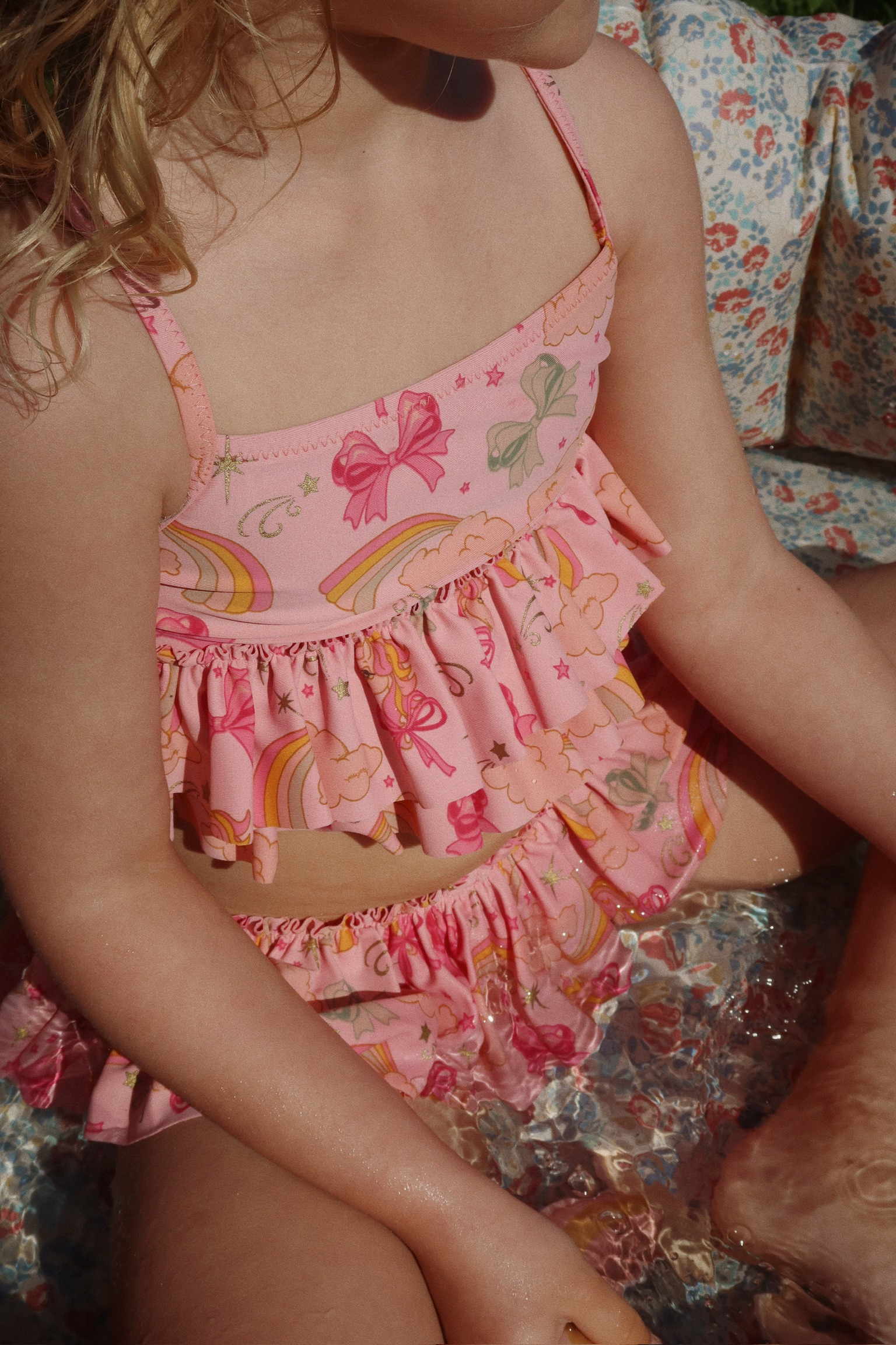 Kinder-Bikini, rosa Farbe, Aufdruck mit Regenbögen, Schleifen und Wolken, Rüschen-Detail.