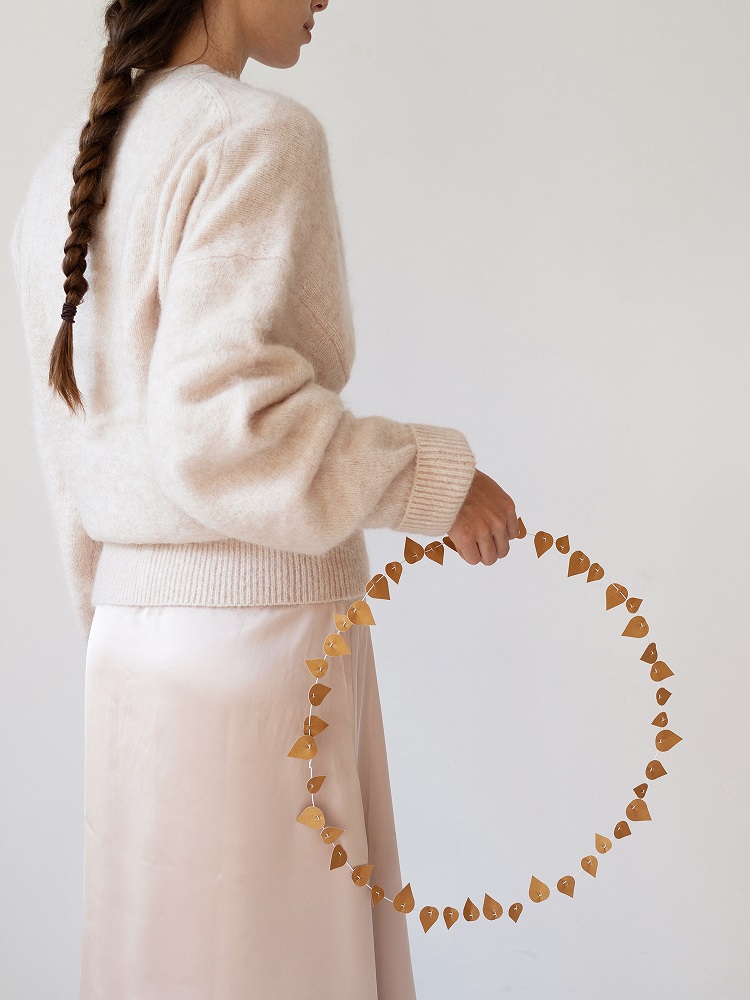 twig-leaves-ochre Strickpullover beige, Rock rosa, Frau mit Zopf, dekorativer Kranz goldene Blätter.