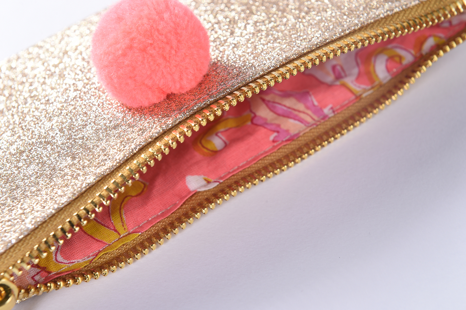 OUSTINA_3 Glitzerndes Etui, goldfarben, Reißverschluss, pinkes Innenfutter mit gelbem Muster, rosa Pompon.