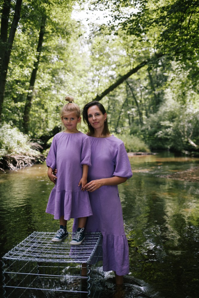 foto-54v6buhbqjxR0R Zwei lila Kleider mit Rüschen, getragen von einer Frau und einem Kind, die auf einem Gitter im Wasser stehen.