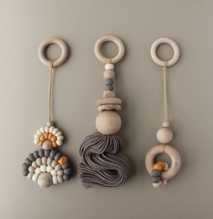 Bildschirmfoto-2019-02-19-um-10-40-17 Drei Holz-Greifringe, beige und naturfarben, hängend; links Regenbogen-Design mit bunten Perlen, Mitte Holzperlen mit Quaste, rechts Ring mit bunten Kunststoff- und Holzperlen; minimalistisch, skandinavischer Stil.