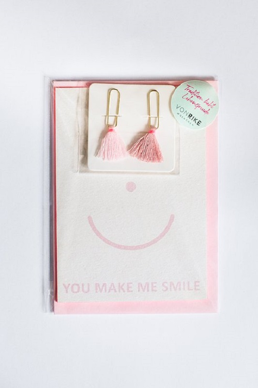 7a75ef_67cf95d14cd64345b2cf960c86f381e2_mv2_d_3107_4656_s_4_2 Ohrringe mit pinken Quasten, goldene Clips, beige Grußkarte, rosa Smiley-Aufdruck, Text "YOU MAKE ME SMILE", transparente Verpackung.