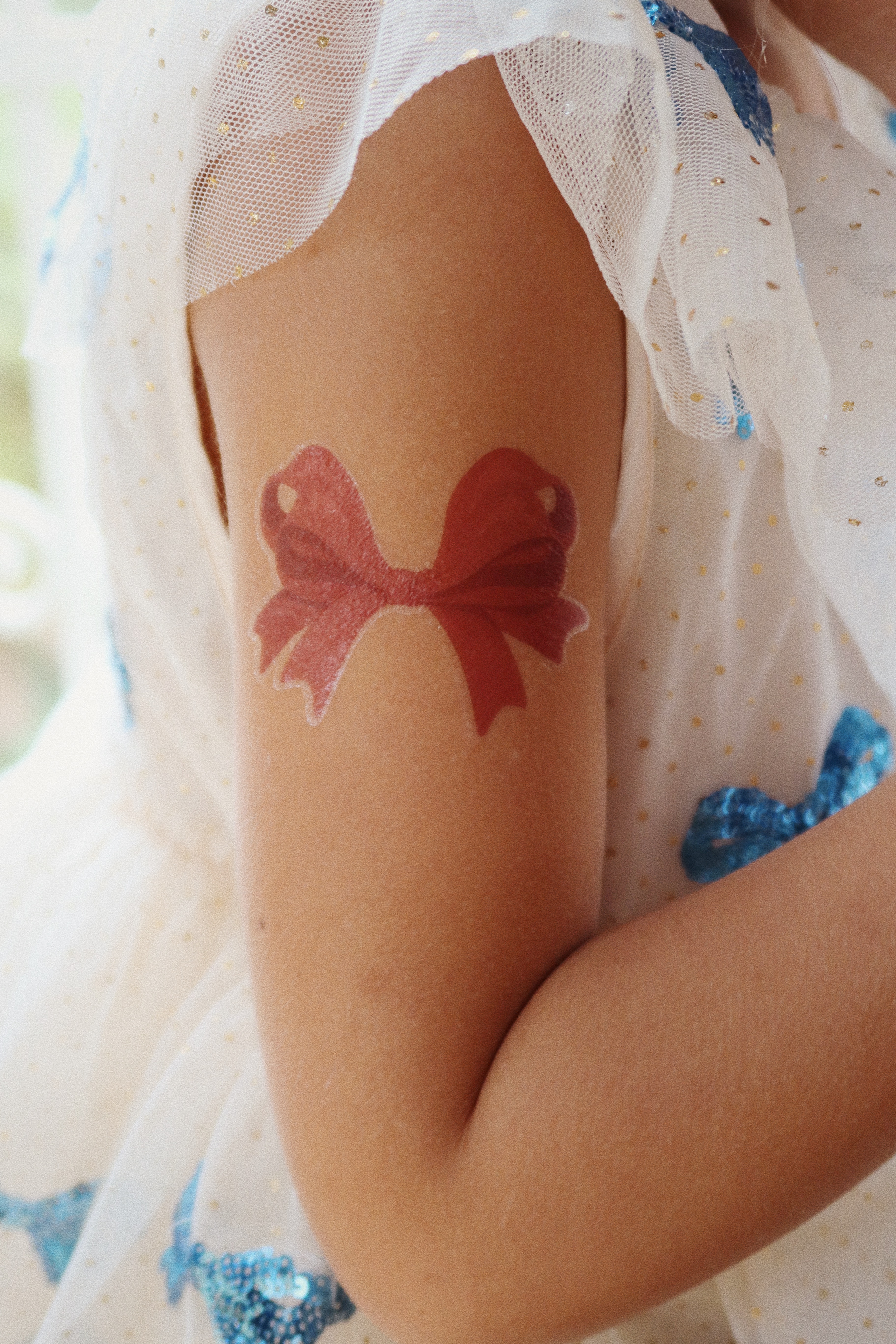 Rotes Schleifen-Tattoo auf Arm, weißes Kleid mit blauen Pailletten und Tüll, Golddetails.