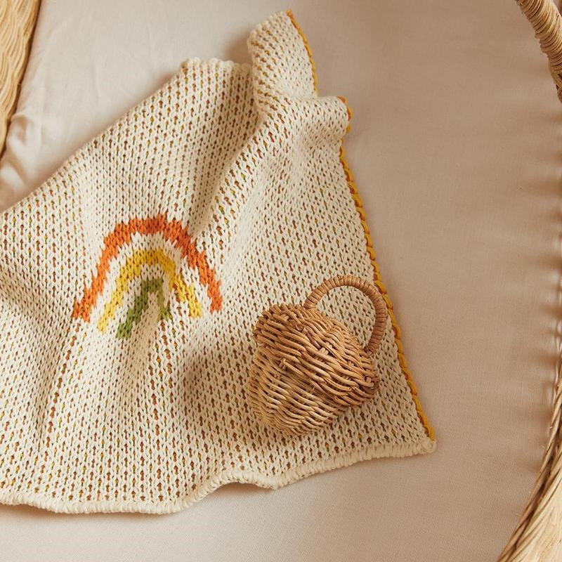 OE-Acorn-Rattle-Rainbow-blanket_800x Babydecke, cremefarben, gestrickt, Regenbogenmuster in Orange, Gelb, Grün; kleiner Korb mit Henkel, braun, rattanähnliches Material.