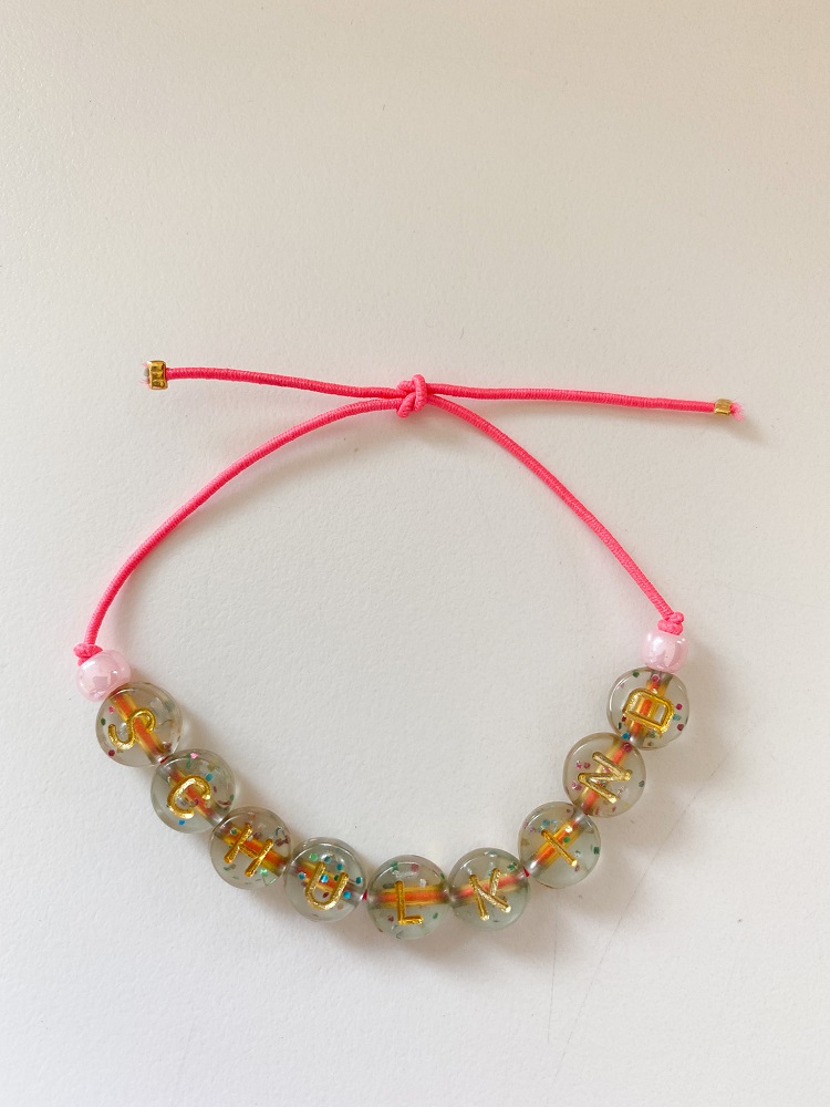 IMG_6793 Armband, pinkes Band, transparente Perlen mit buntem Glitter und goldenen Buchstaben, Knotenverschluss.