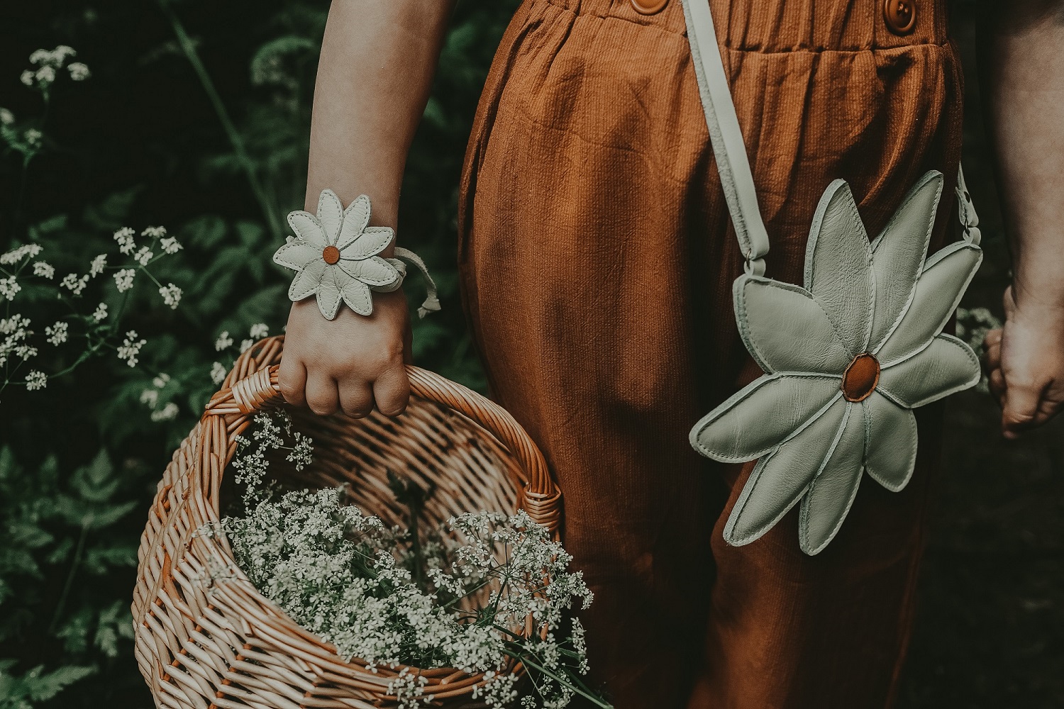 5003004_LE060_22 Blumengeldbörse, weiß mit orangefarbener Mitte, passendes Armband, gewebter Korb mit weißen Blumen, braune Hose.