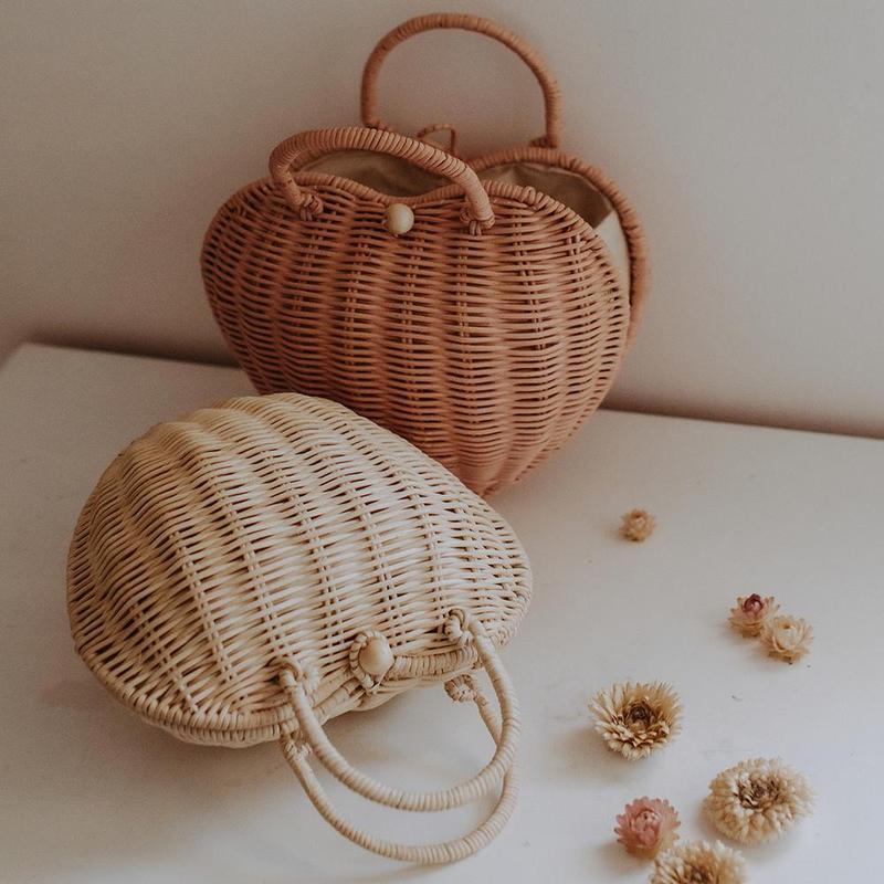 OlliElla-LuvyaBag-Rose-Straw-Lifestyle-web-01_800x Zwei handgefertigte Rattan-Taschen, herzförmig; eine in Natur, die andere in Braun; beide mit kurzen Griffen und Knopfverschlüssen.