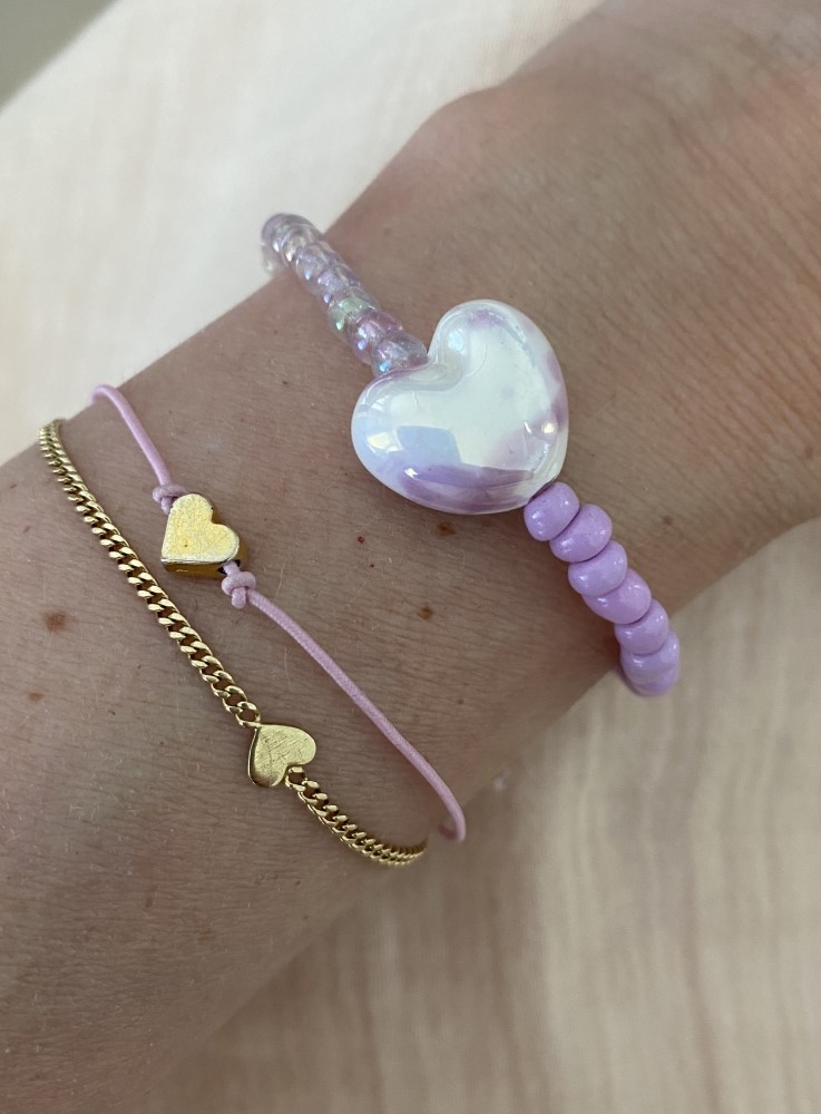 IMG_1360 Drei Armbänder; goldenes Kettchen mit Herzanhänger, rosa Band mit kleinem Herz, lila Perlenarmband mit großem schimmerndem Herz.