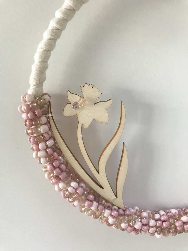 IMG_3617 Handgefertigter Dekokranz, verziert mit Holzblume und pastellfarbenen Perlen in Rosa und Beige, umwickelt mit beigem Stoffband.