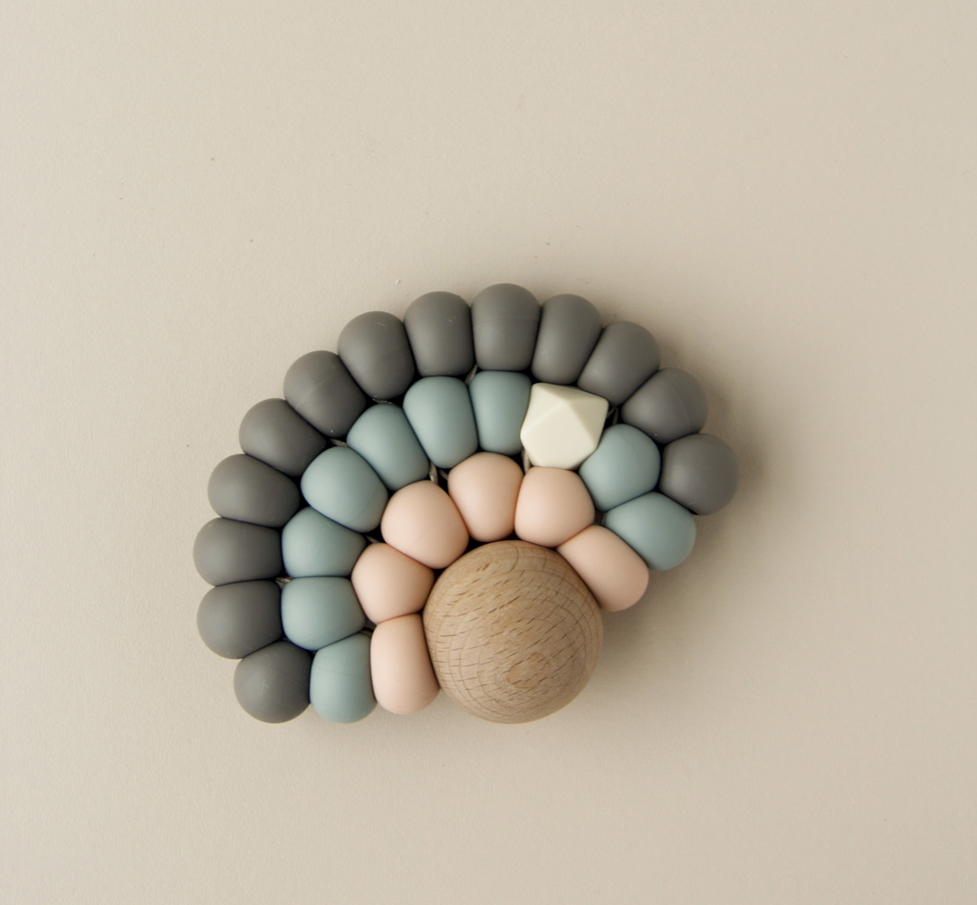 _MG_1070 Beißring aus Holz und Silikon, Halbkreisform, Perlen in Grau, Blau, Rosa, Weiß, Holzstruktur.