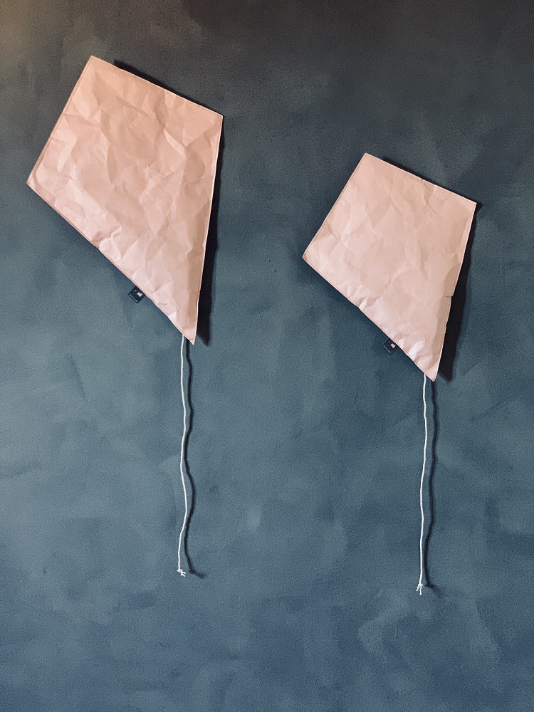 IMG_5854 Papierdrachen-Set, zwei Stück, rechteckige Form, rosa, mit Schnüren, an Wand angebracht.