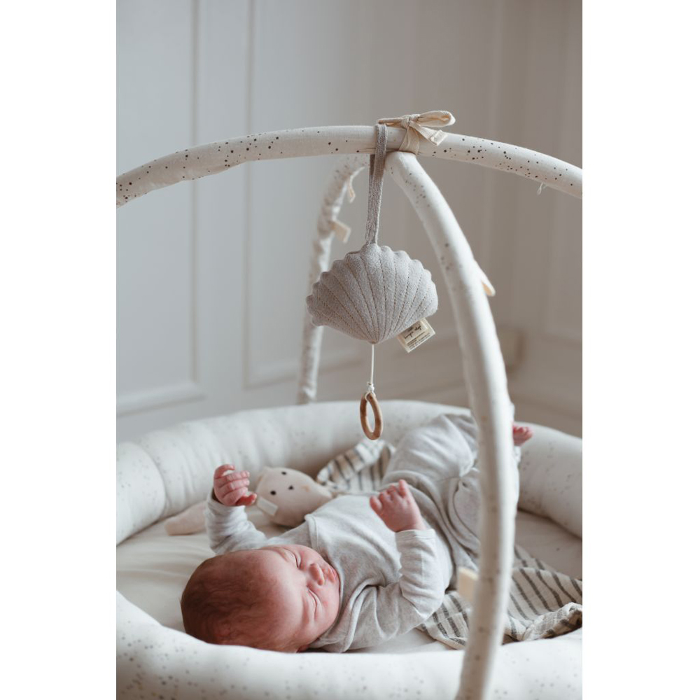 KS1033-Extra-4 Babygym, cremefarben, gepunktete Bögen, hellgraue Stoffmuschel mit Holzring, beige gepunktete Babydecke, Baby in grauem Strampler.