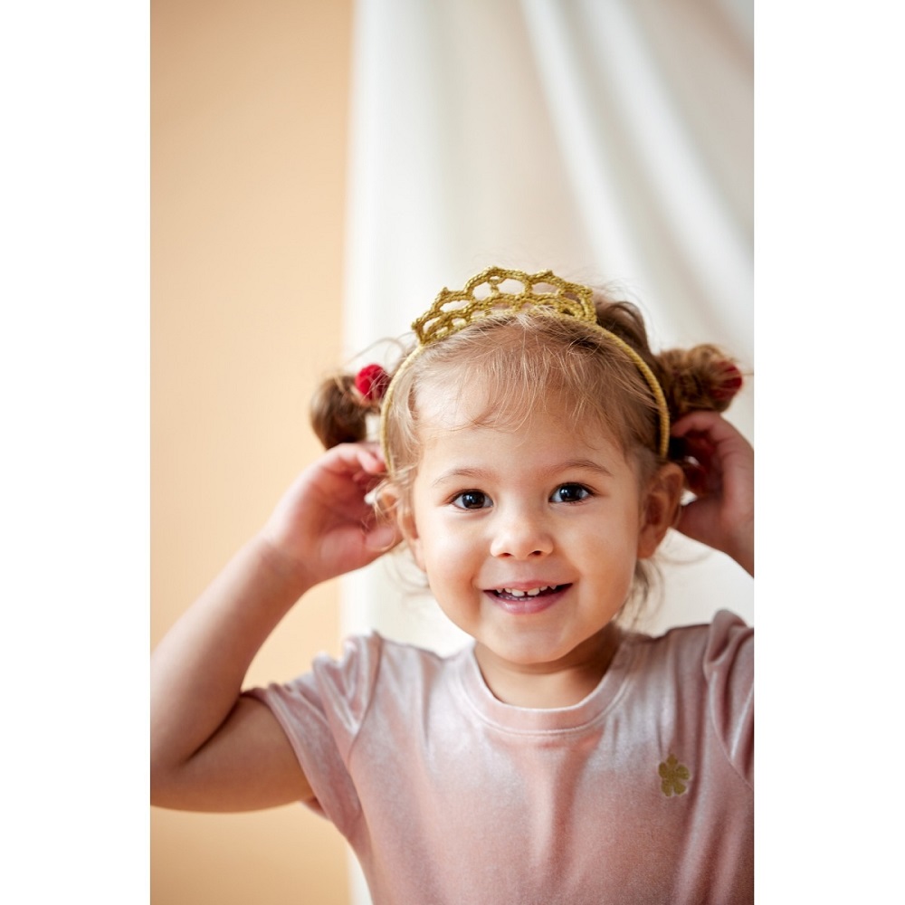 9511178-Haarreif-Krone-gold-2 Kind mit goldener Krone, rosa Samtshirt, kleeblattförmiger Aufdruck, blonde Haare, lächelnd.