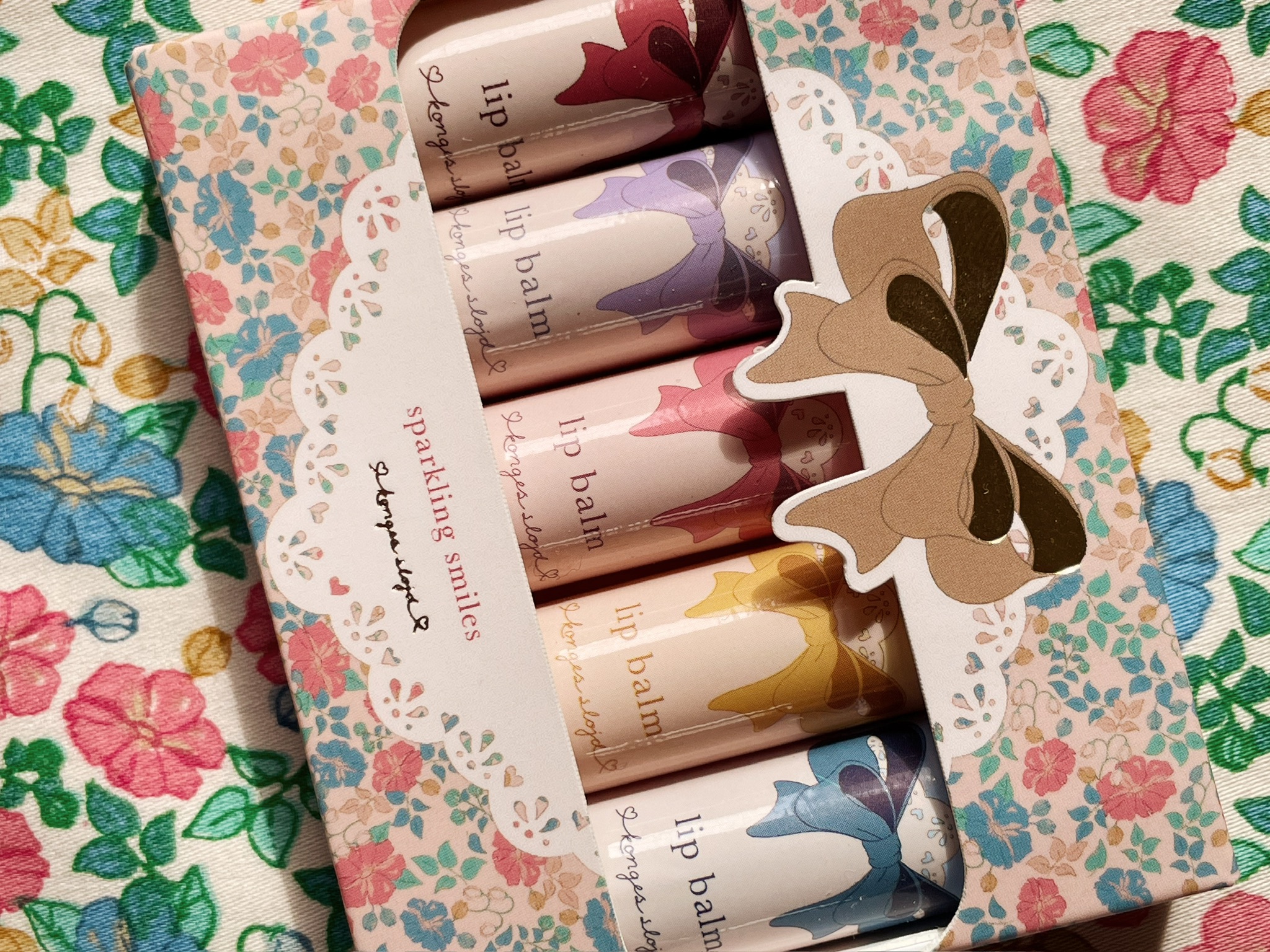 Lippenbalsam Set, fünf Stück, Pastellfarben, jeweils Farbbänder-Aufdruck in Rot, Lila, Rosa, Gelb, Blau, florale Verpackung mit Schleife, Marke Konges Sløjd.