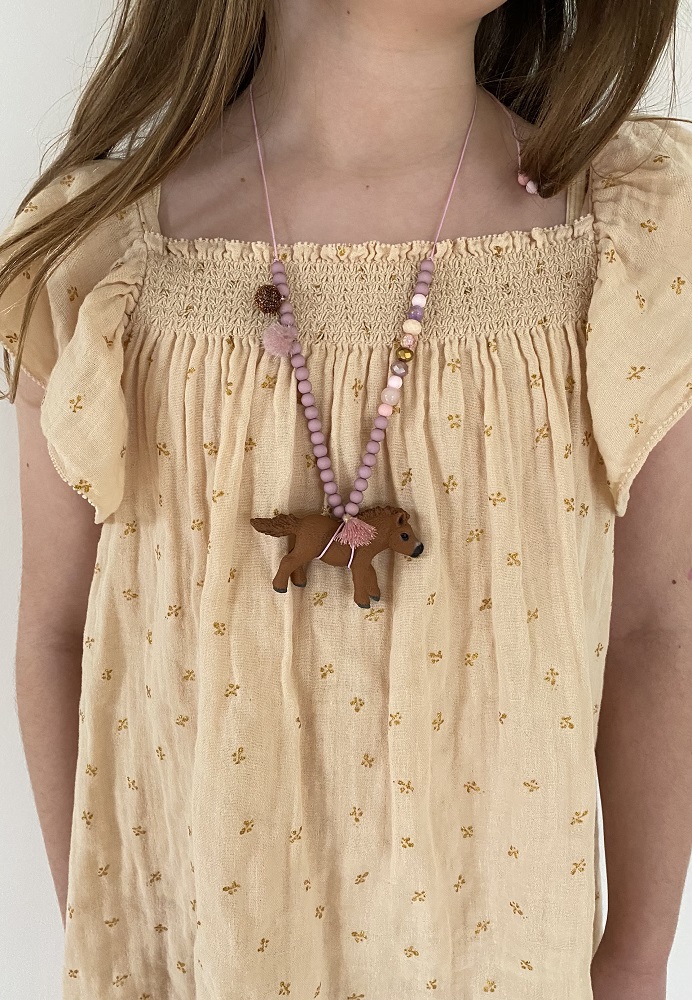 IMG_5075 Kette aus rosa Perlen, Anhänger in Form eines braunen Hundes, Mädchenkleid beige mit gelbem Blumenmuster.