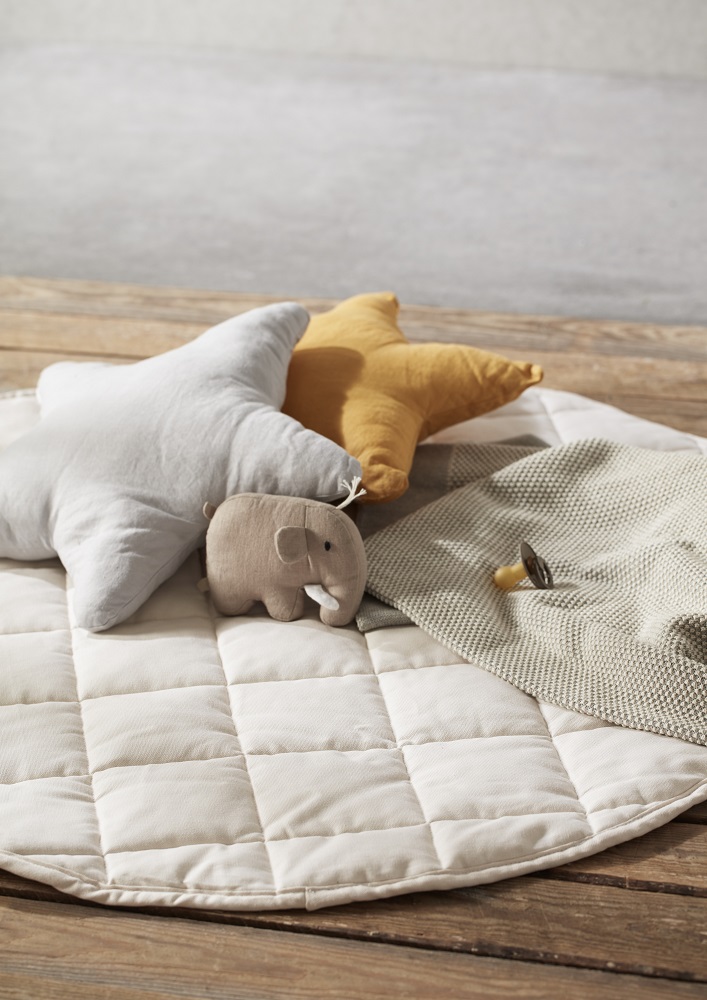1000483-Play-mat-Beige-E_5 Beige Babyspielmatte, zwei sternförmige Kissen in Weiß und Gelb, kleines Elefantenspielzeug aus Stoff, beigefarbene Strickdecke, Holzuntergrund.