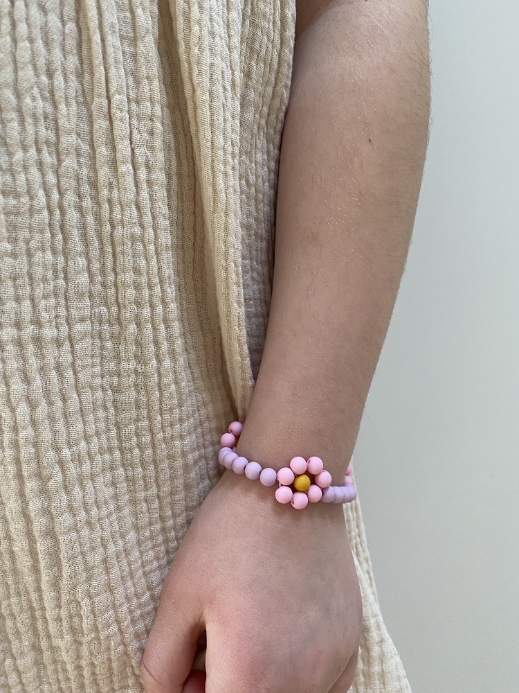 IMG_4906 Armband, rosa Perlen, gelbe Blumenform, am Handgelenk, beiger Stoffhintergrund.