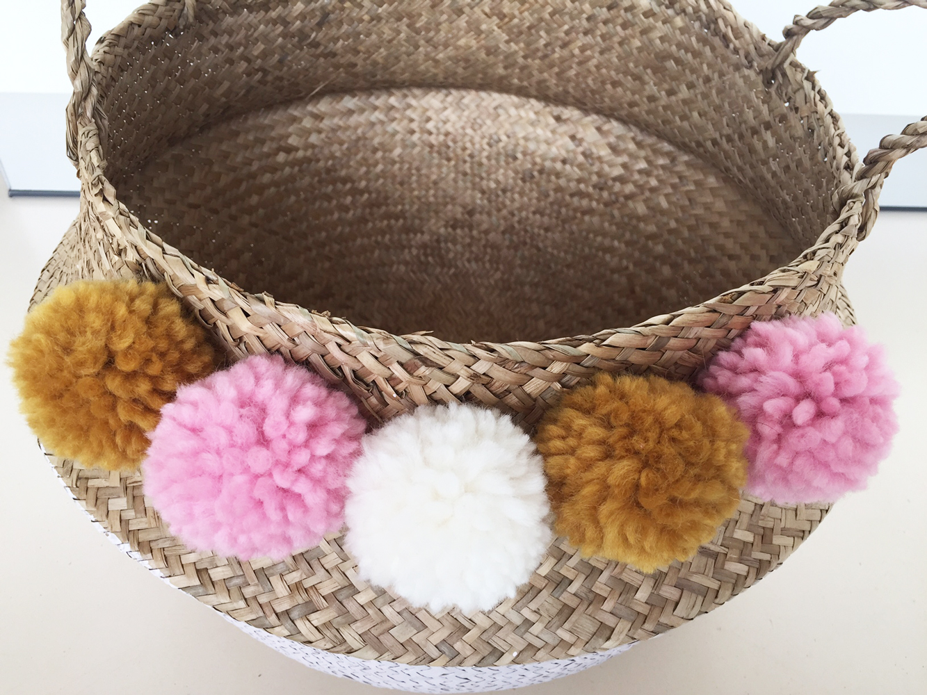 IMG_8926 Korb, geflochten, naturfarben, dekoriert mit Pompoms in Rosa, Weiß, Gelb, Henkel, runde Form.