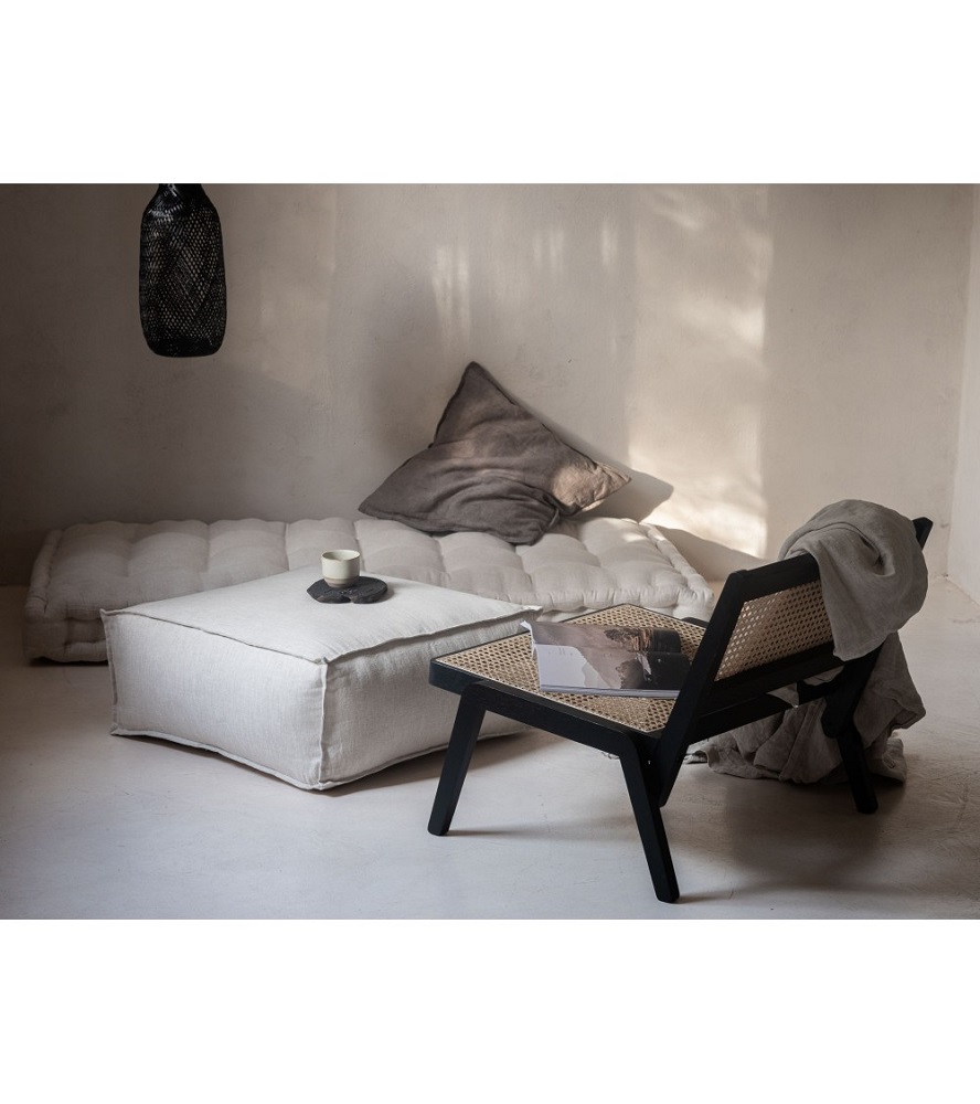 lniany-puf-podlogowy-naturalny-bez-2 Sitzgruppe mit hellen Kissen und Pouf, schwarzer Sessel mit geflochtener Sitzfläche, graue Decke, helle Tasse auf Pouf, minimalistisches Design.