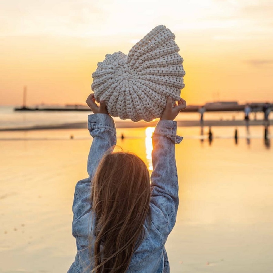 il_794xN-2828080412_2jwygFhgtEqJNBm6j Gehäkeltes Kissen, Muschelform, cremefarben, grobes Muster, gehalten von Person in Jeansjacke.