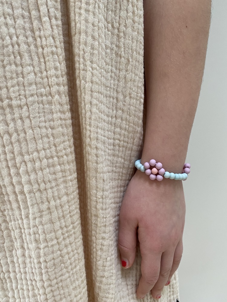 IMG_4921 Armband, Perlen, Farben: Rosa, Hellblau, Blumenmuster, getragen am Handgelenk, beige Stofftextur im Hintergrund.