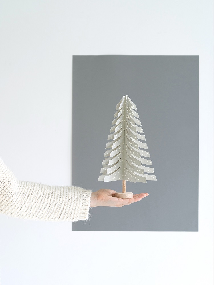 fir-tree-light-grey Papier-Weihnachtsbaum, weiß, perforierte Muster, Holzstamm, Hand hält Baum, grauer Hintergrund.