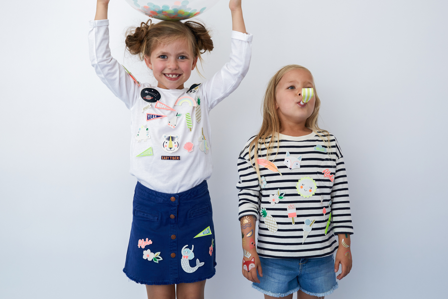 Everyday17-Access-981-E15971bf9c2728e Kinderbekleidung; links: weißes Langarmshirt, bunte Aufnäher, blauer Rock; rechts: gestreiftes Langarmshirt, bunte Aufnäher, kurze Jeans; bunte Aufkleber auf Armen und Gesicht