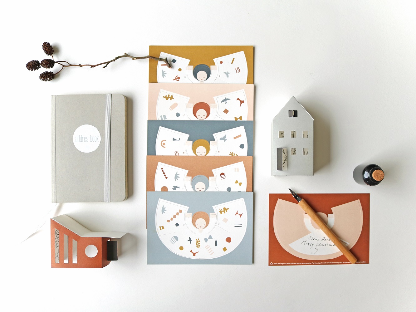 fridur-new-33 Notizbuch beige, Umschläge in Senfgelb, Rosa, Petrolblau, Terrakotta mit minimalistischen Gesichtsmotiven, Papierhaus, Tintenfass, Federhalter auf Karte.