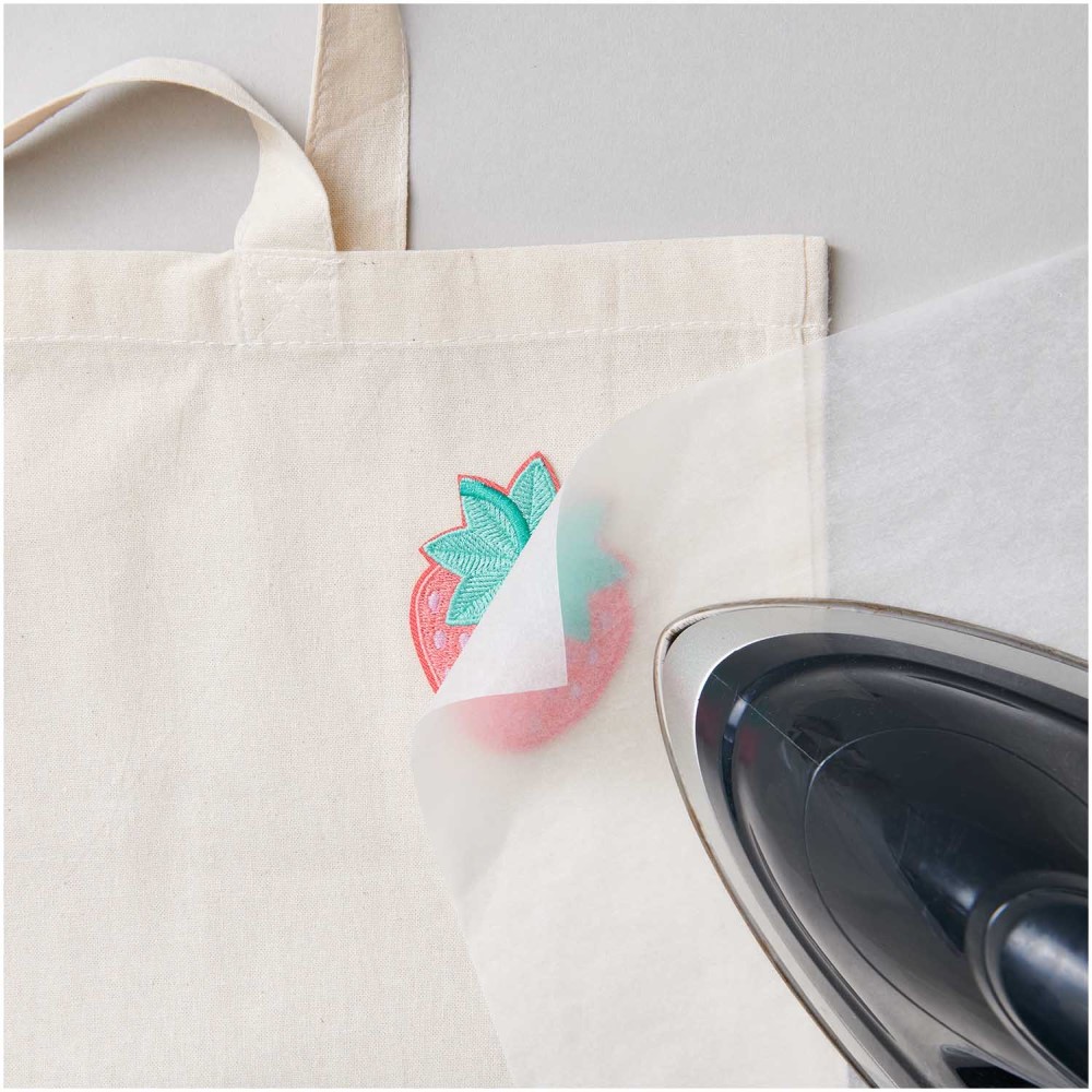 280084_aw_2 Beutel aus Baumwolle, naturfarben, Erdbeeraufdruck in Rot und Grün, Heißtransferverfahren, transparentes Bügelpapier, Bügeleisen teilweise sichtbar.