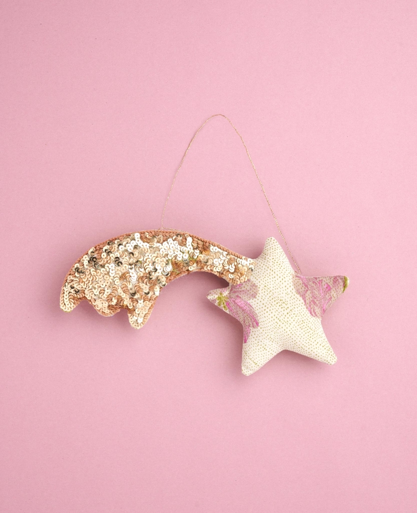 Shooting-Star-SILK-Ornament-Sand Weihnachtsanhänger, Sternform, cremefarben, glitzernde Pailletten, pinke Akzente, goldener Schweif, rosa Hintergrund.