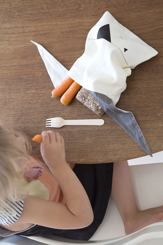 lunchbag-pirate-2 Stoffserviette mit Panda-Aufdruck, helles Beige, gefüllt mit Karotten und Brot, Holzspork daneben, Kind im Hintergrund.