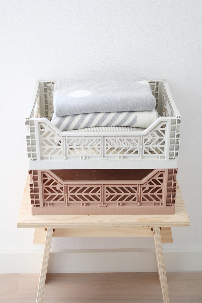 lillemor_lifestyle_productshot_010 Klappkisten, gestapelt, obere Kiste cremefarben, untere Kiste braun, enthalten graue Decken mit weißen Mustern, Holzbank.