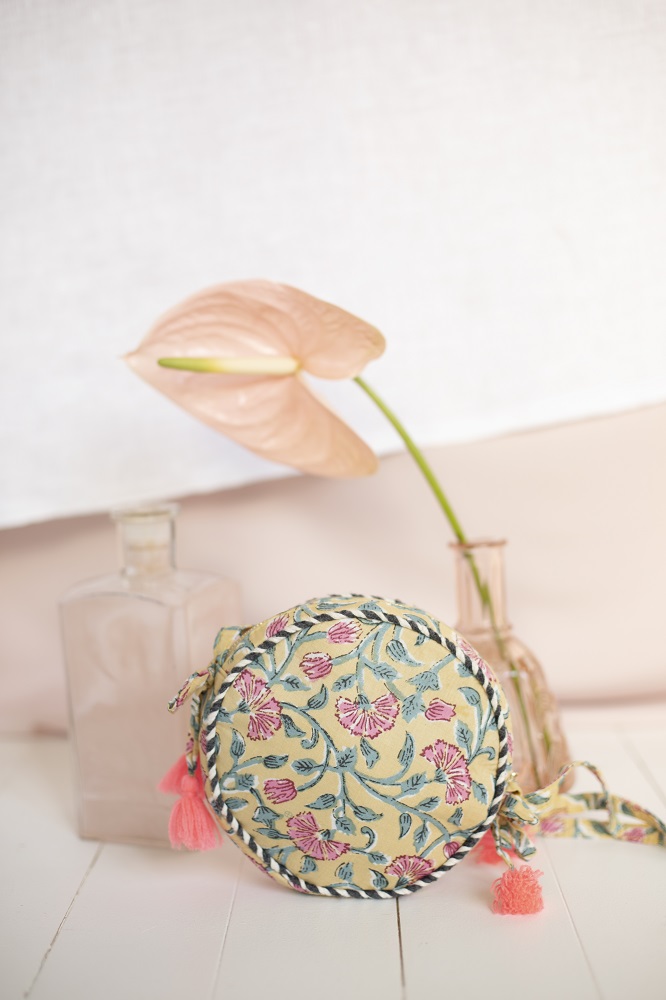 girls-bag-suzy-lemon-flowers-1 Runde Tasche, florales Muster, beige Hintergrund, rosa Blumen, hellblaue Blätter, pinke Quasten, geflochtener Rand, Stoffmaterial.